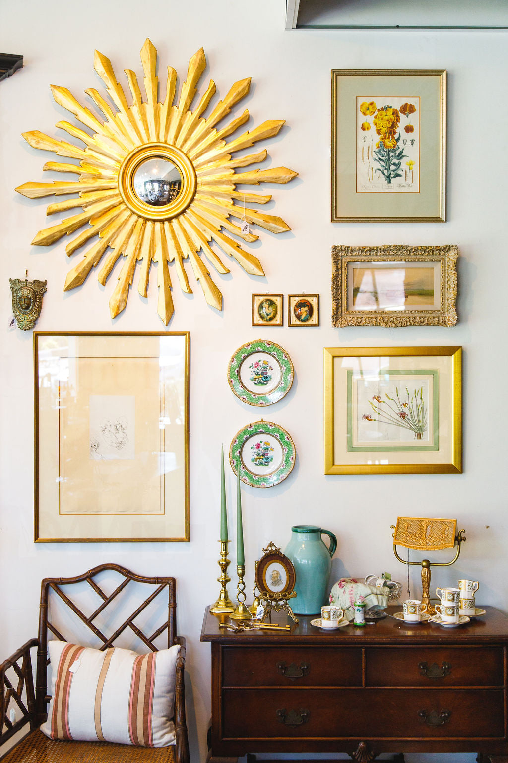 Decorative wall with sunburst mirror, framed art, and a wooden dresser.