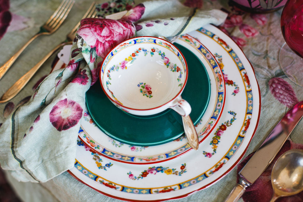 Decorative table setting with floral teacup and saucer on a patterned plate.